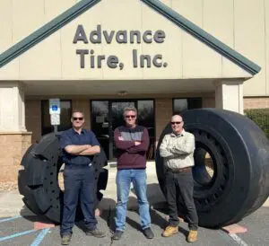 Three men standing in front of a building with large tires.